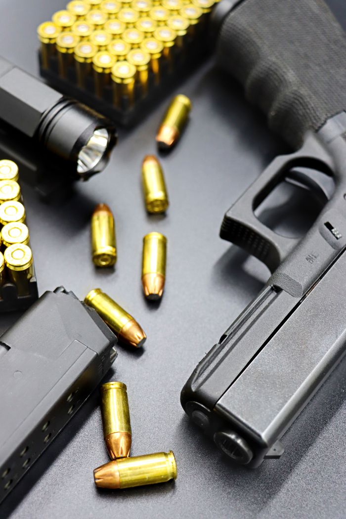 Home Detailed view of a black handgun with bullets and ammo clips on a black surface, showcasing firearm elements.